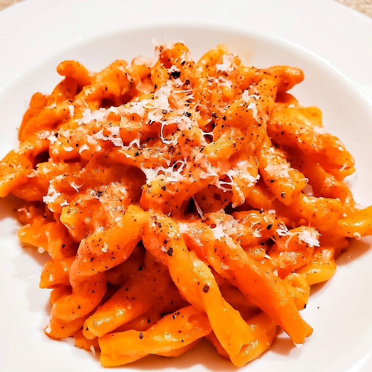 A plate of rotini pasta coated in sauce and topped with Parmesan cheese and black pepper.