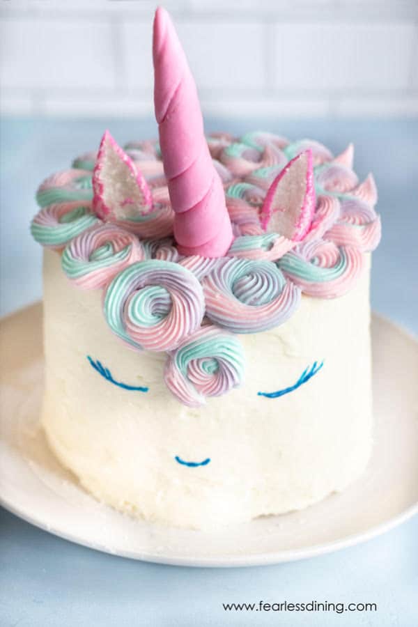 White unicorn cake with a pink horn made of Peeps marshmallow fondant and swirls of frosting for its mane.