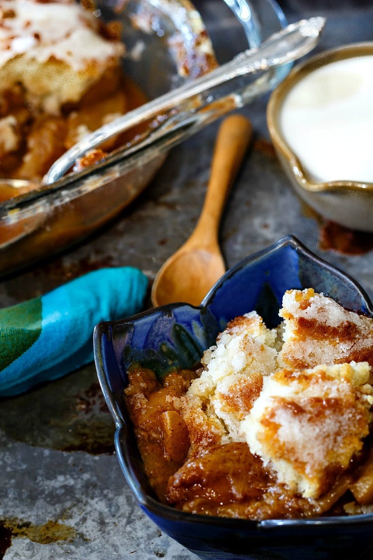 blue bowl of spiced peach sonker with the casserole dish of lazy sonker in the background