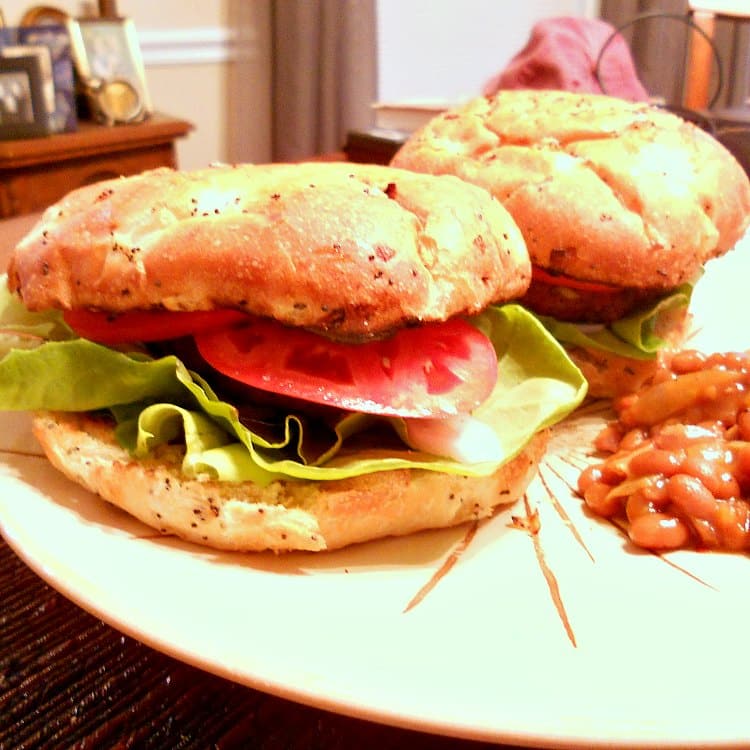 Two burgers on a plate with lettuce and tomatoes.