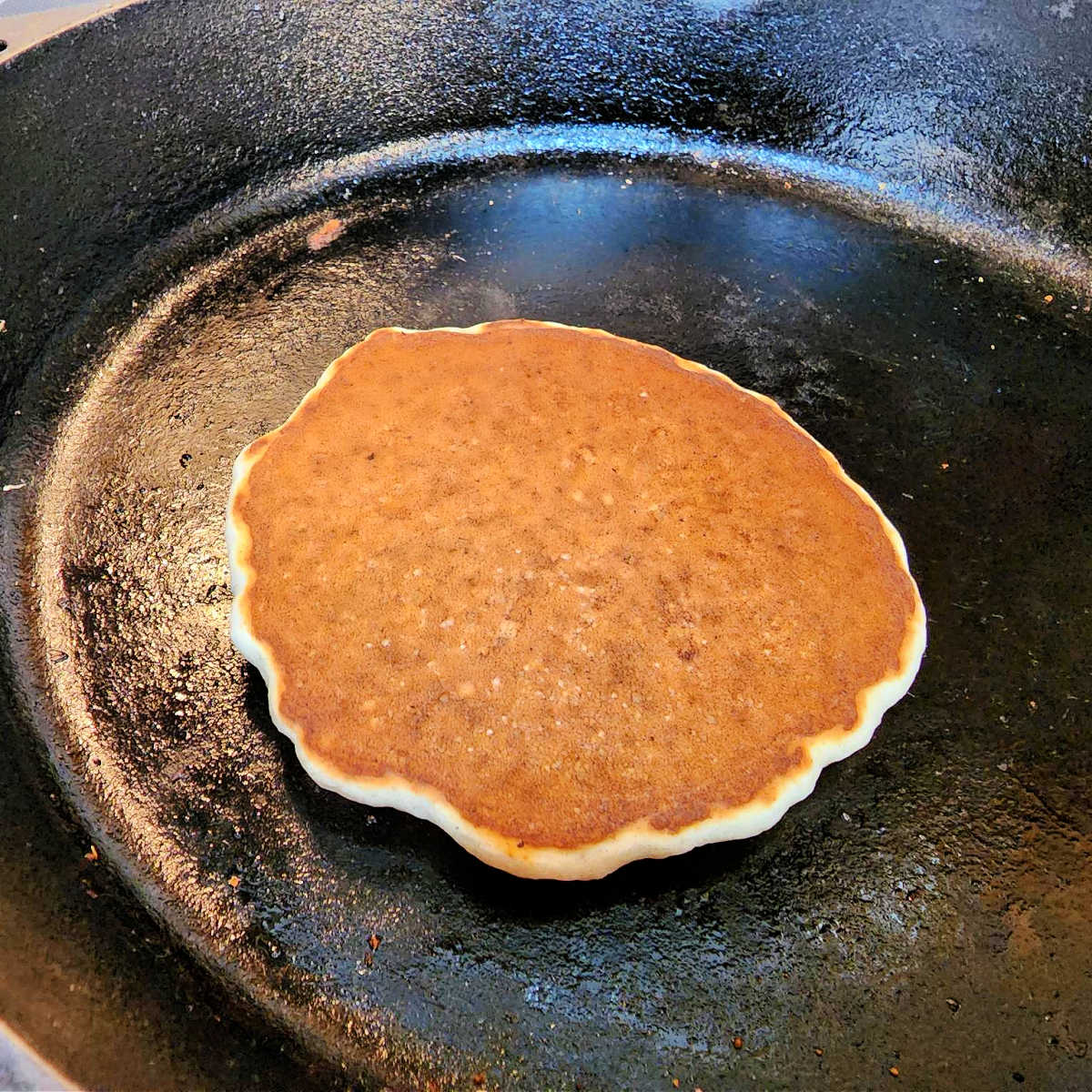 Close-up of a pancake in a cast iron skillet after it has been flipped. The pancake is an even, deep golden-brown.