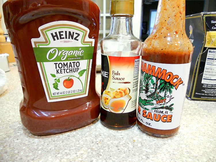 A bottle of ketchup, a bottle of fish sauce, and a bottle of Gator Hammock hot sauce on a counter.