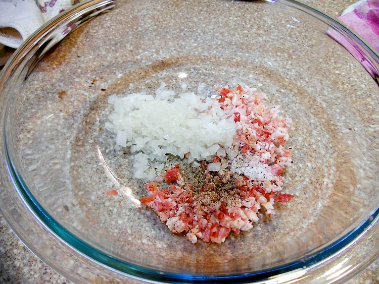 A glass bowl with minced onion, minced raw bacon, and black pepper in it.