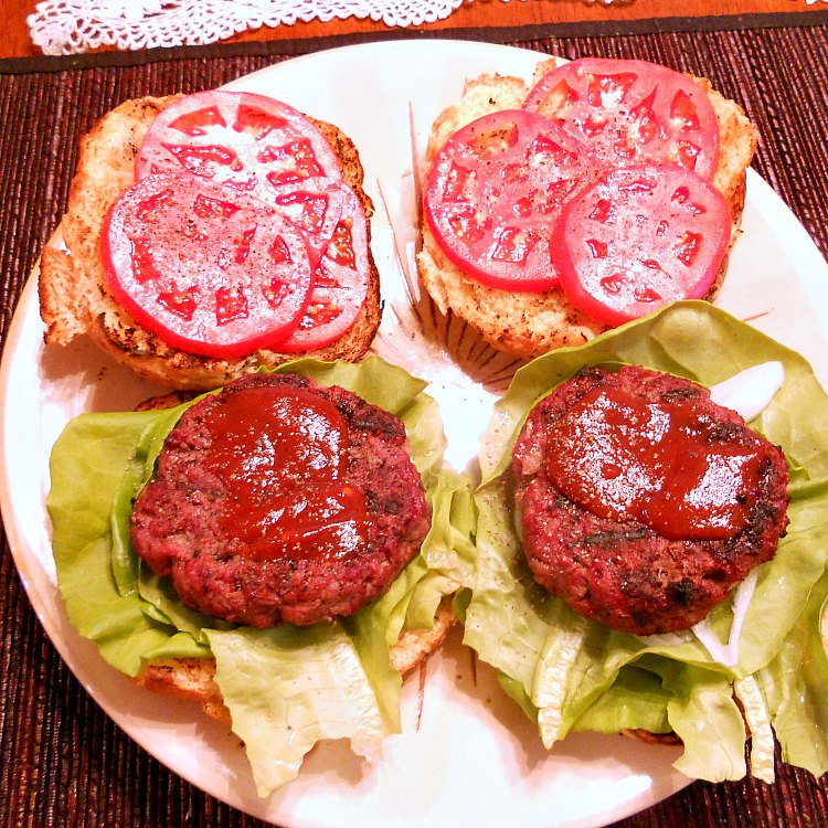 2 bison burgers on lettuce with the buns open to show the sauce and sliced tomatoes.