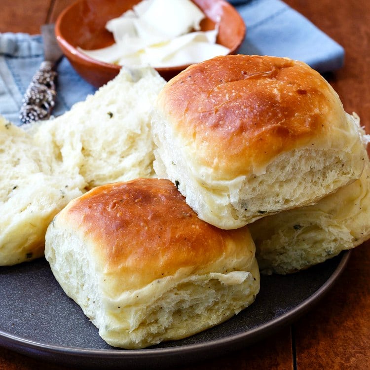 A plate of four dinner rolls, one split open, with a dish of butter.