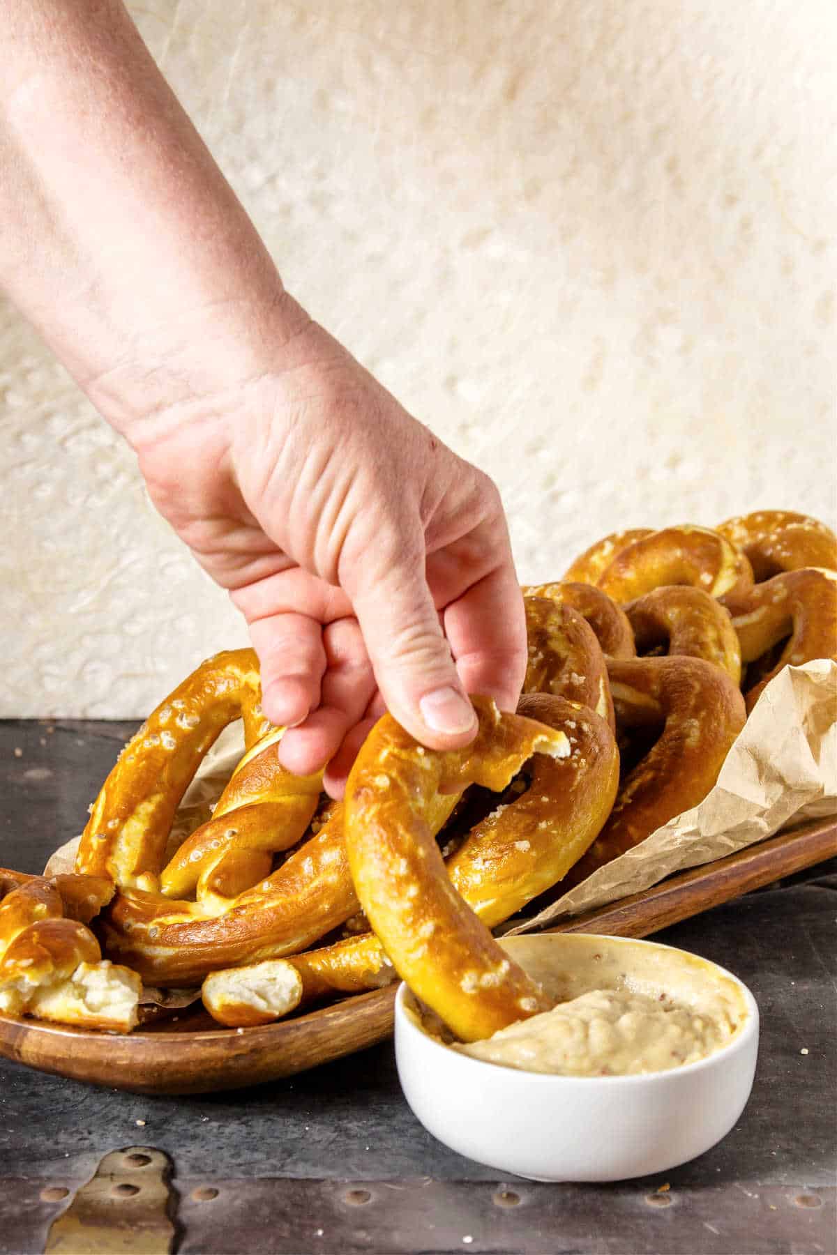 A hand holding a bread pretzel and dipping it into a small white bowl of beer cheese.