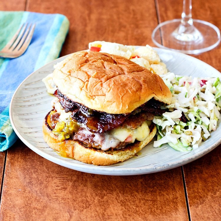 A smashed cheeseburger with bacon served on a plate with coleslaw and pasta salad.