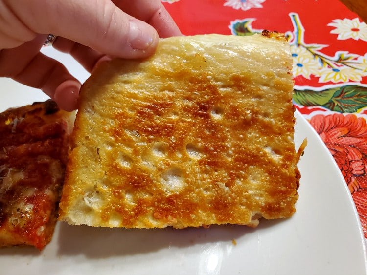 Underside of a slice of grandma pizza showing the burnished golden brown fried bottom crust.