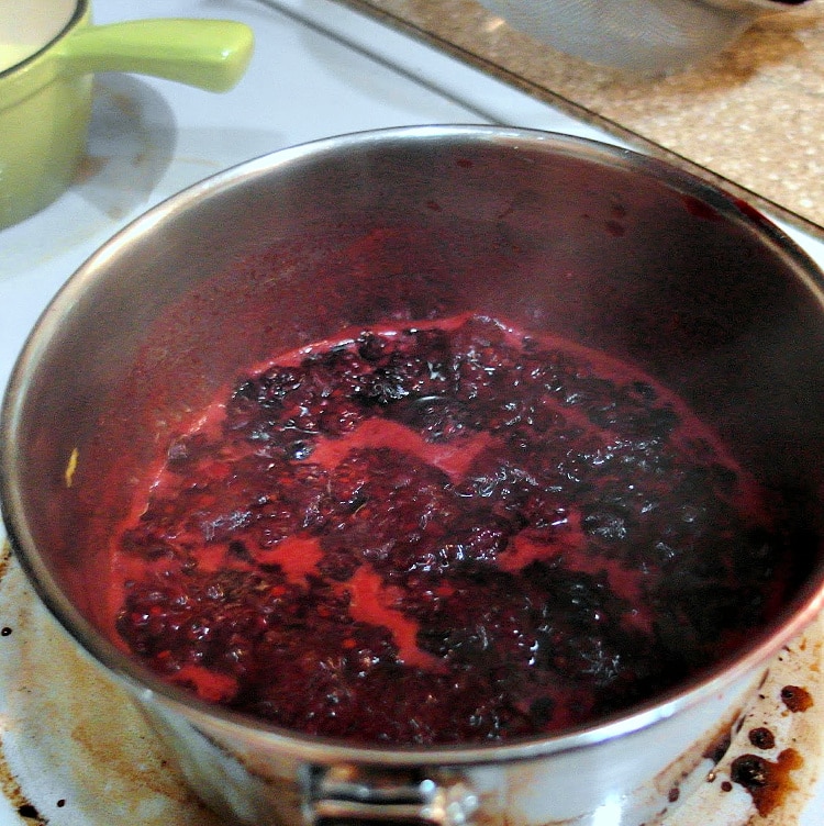 A sauce pan full of blackberry puree reducing on the stove.