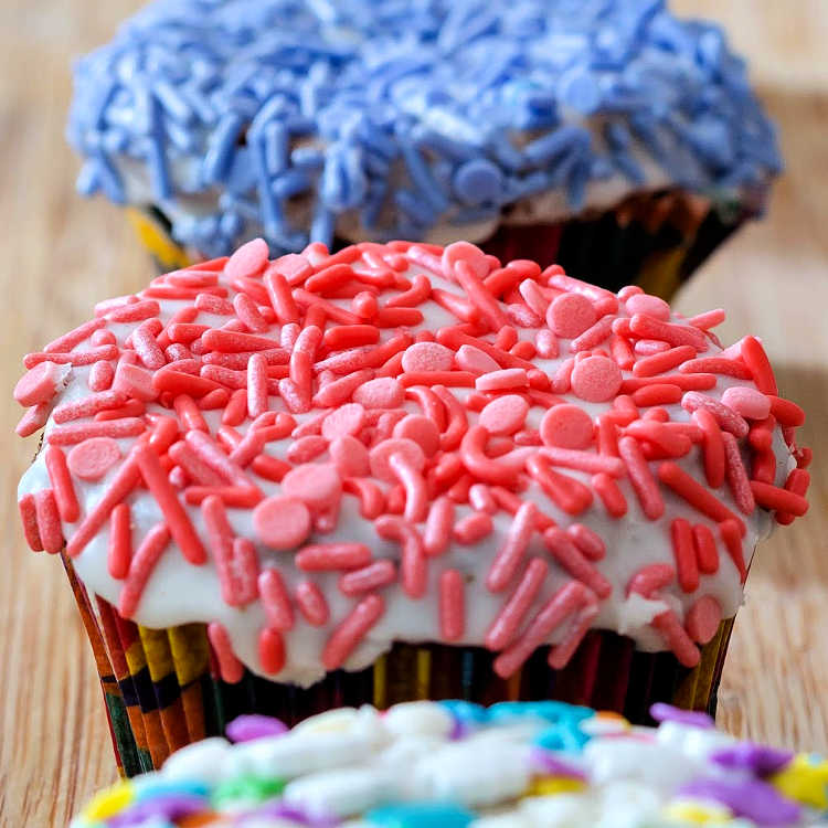 Close up shot of brown sugar cinnamon pound cake baked as cupcakes with a glazed top and covered in pink sprinkles, blue sprinkles on cup cake in the background.