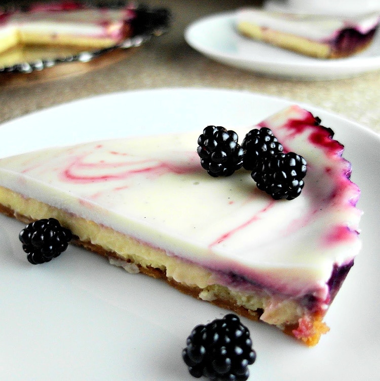 A side view of a slice of blackberry swirl cheesecake tart on a white plate and garnished with whole fresh blackberries.