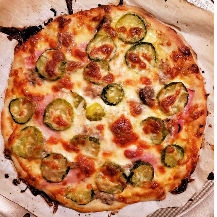 A round pizza with pickles, ham, pork, and swiss cheese baked and ready to serve.