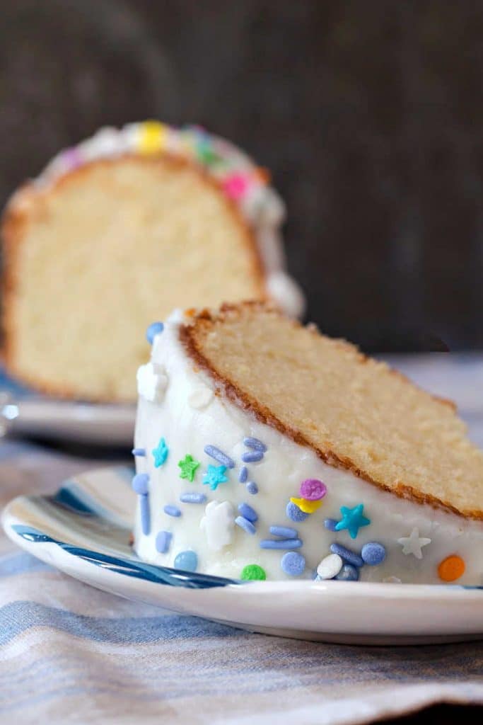 A slice of cake with white glaze and multi-colored sprinkles.