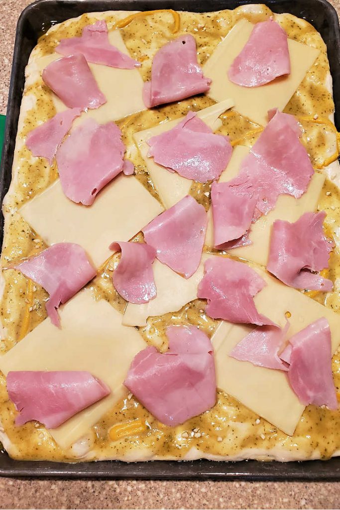 Piles of shaved ham placed on swiss cheese on a cubano pizza dough.