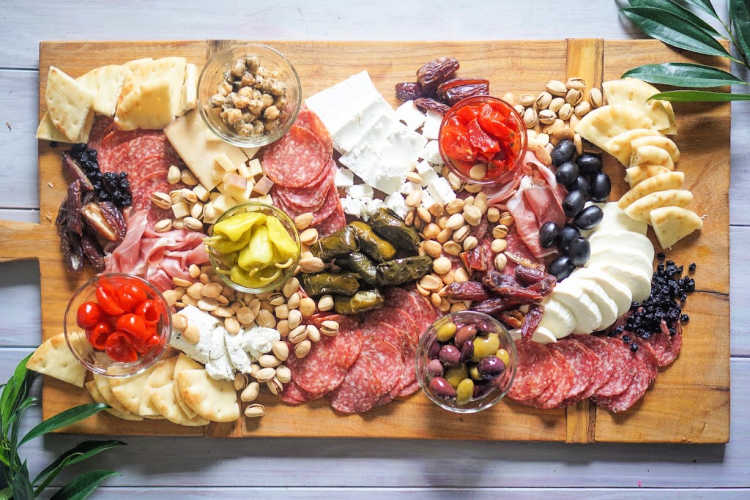 A whole cheese board with meats, nuts, cheeses, olives, and crackers.