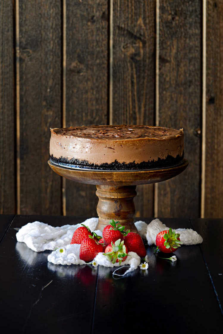A whole Nutella cheesecake on a wooden pedestal with fresh whole strawberries around the base.
