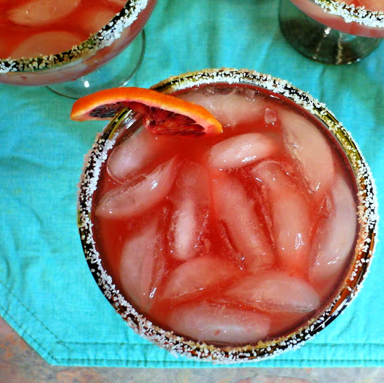 Top down view of blood orange margarita over ice in a salt rimmed glass, garnishes with a blood orange.