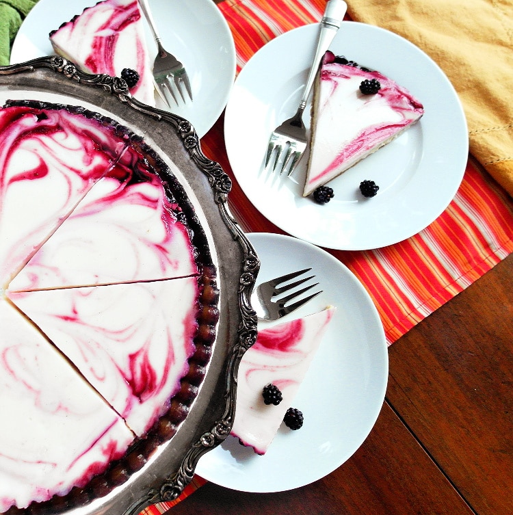 A sliced cheesecake tart shot from above on a sliver platter with individual servings on white plates on the side.