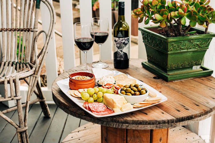 A cheese board with 2 glasses of wine, ready for serving on a porch.