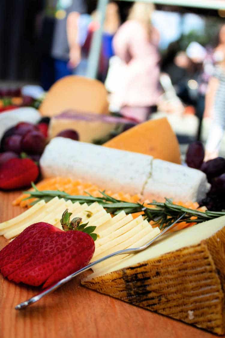 A log of goat cheese, a wedge of hard cheese and slices of cheese with a sliced strawberry and herbs on a board.