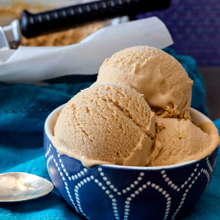 A blue bowl of creamy butterscotch ice cream on a blue napkin.