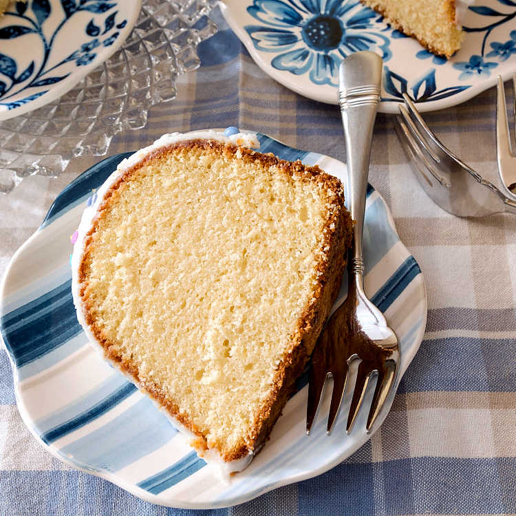 A slice of pound cake on a blue and white striped plate with a silver fork ready for serving.