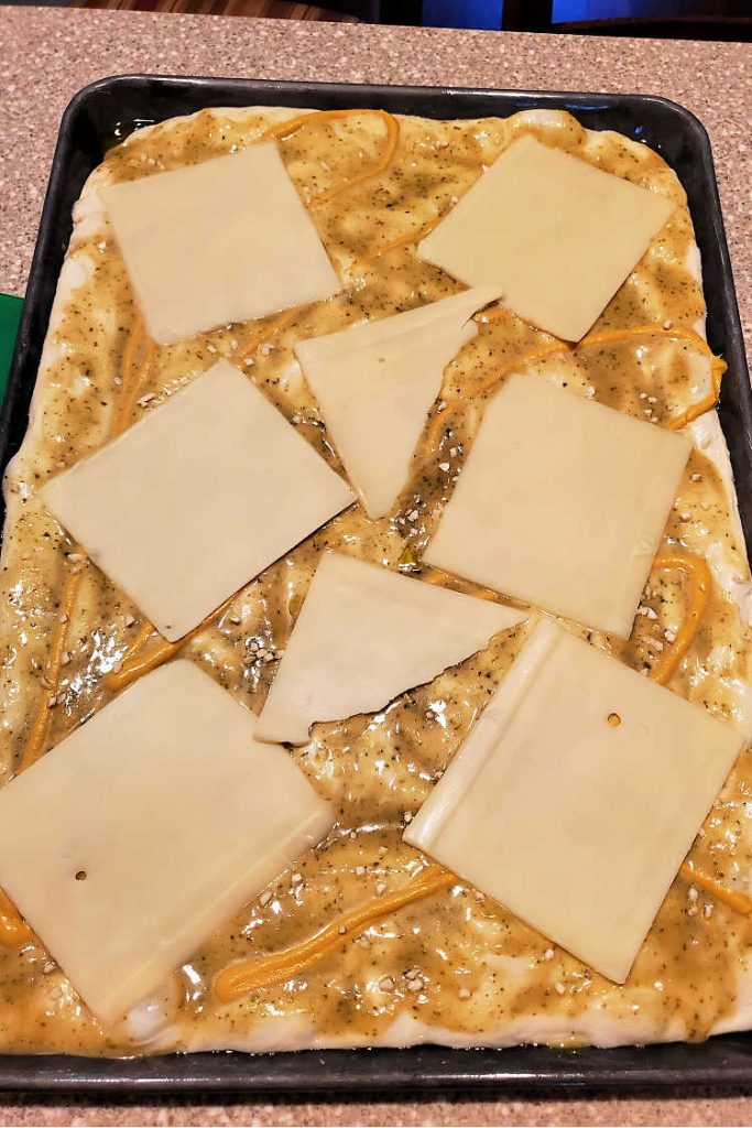 Slices of Swiss cheese on mustard-covered pizza dough before baking.