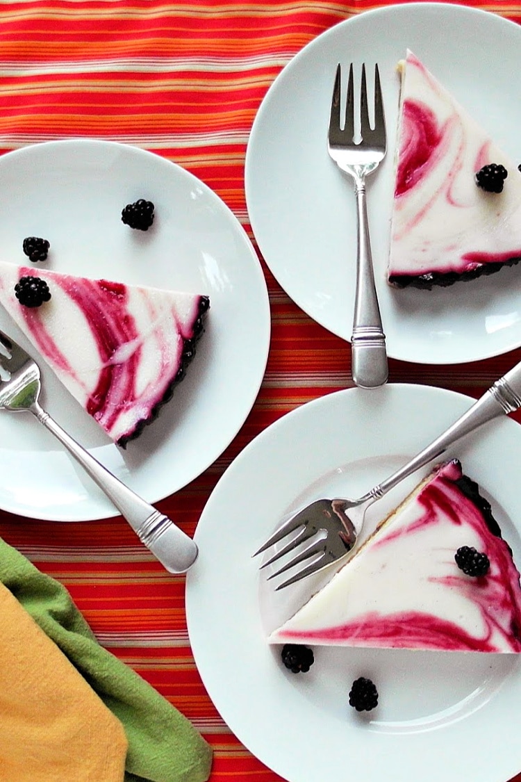 3 slices of blackberry swirl cheesecake tart on 3 white plates with forks, ready for serving.