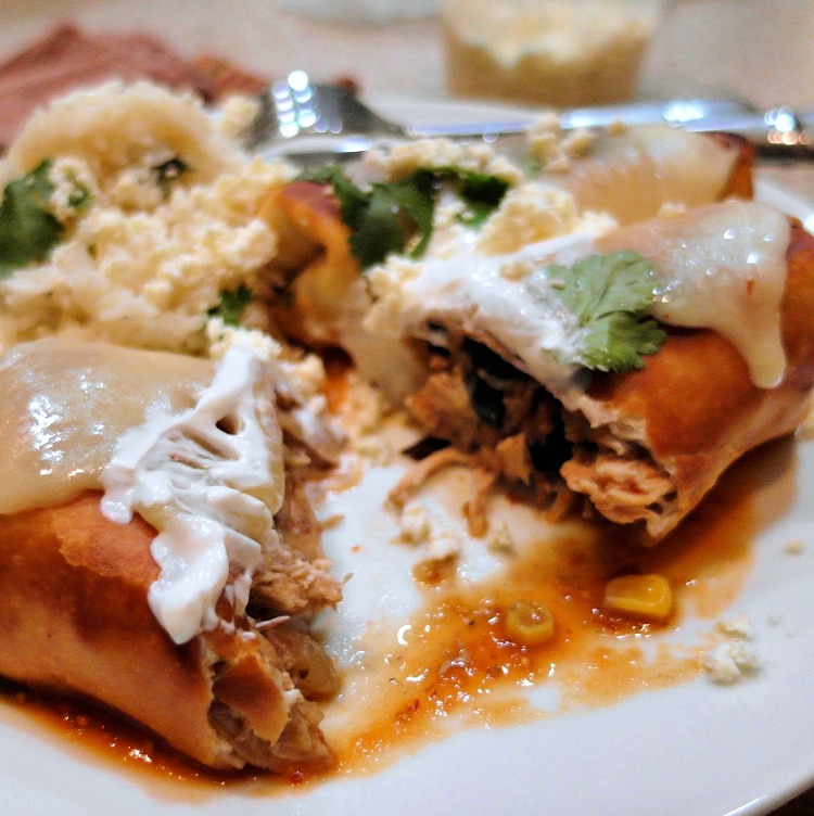 A chicken chimichanga with melted cheese and sour cream cut open so you can see the filling.