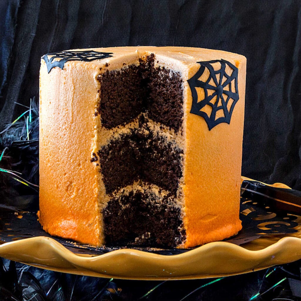 A three layer chocolate Halloween cake with a slice cut out of it, showing three layers of dark chocolate cake inside.