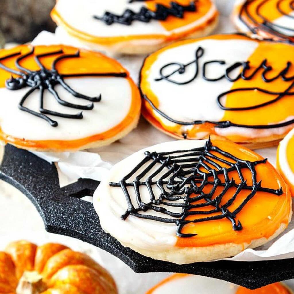 A tray of orange and white iced cookies with spider decorations. Text on one of them reads "Scary".