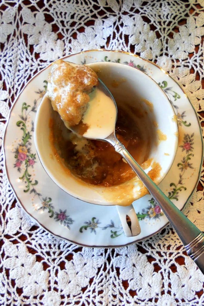 Overhead shot of a teacup on a saucer with pudding chomeur in it and a spoonful ready to eat.