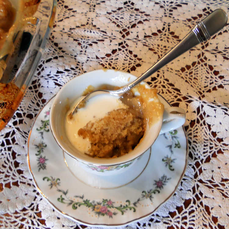 A teacup of pudding chomeur with heavy cream poured on it.