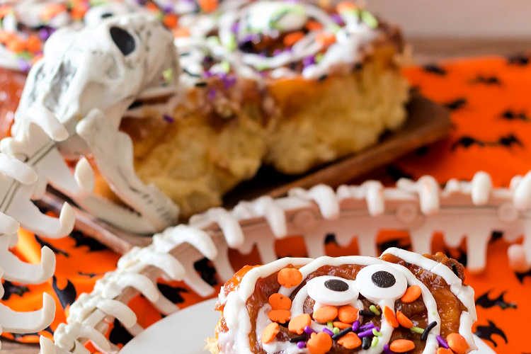 a cinnamon roll decorated for Halloween on a plate with a plastic snake skelteon