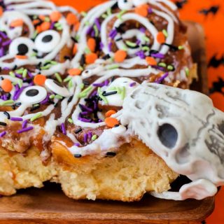 snake skull taking a bite out of halloween decorated cinnamon rolls on a plate