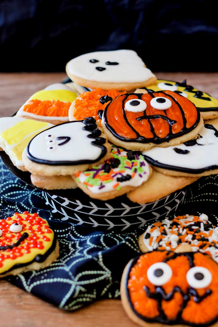 Lots of decorated Halloween shortbread cookies on a spider web-printed cloth background.