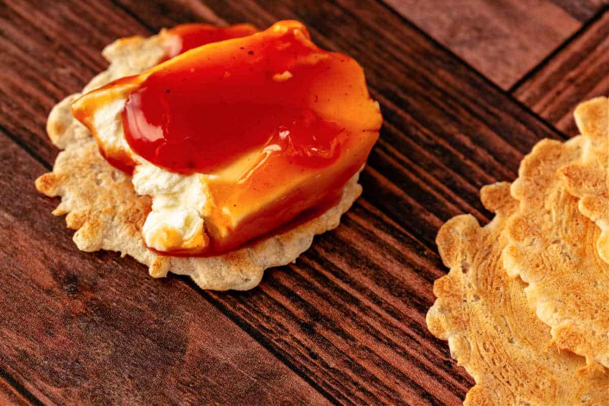 An extreme closeup of a round cracker topped with cream cheese and tangy red sauce on a wooden surface.