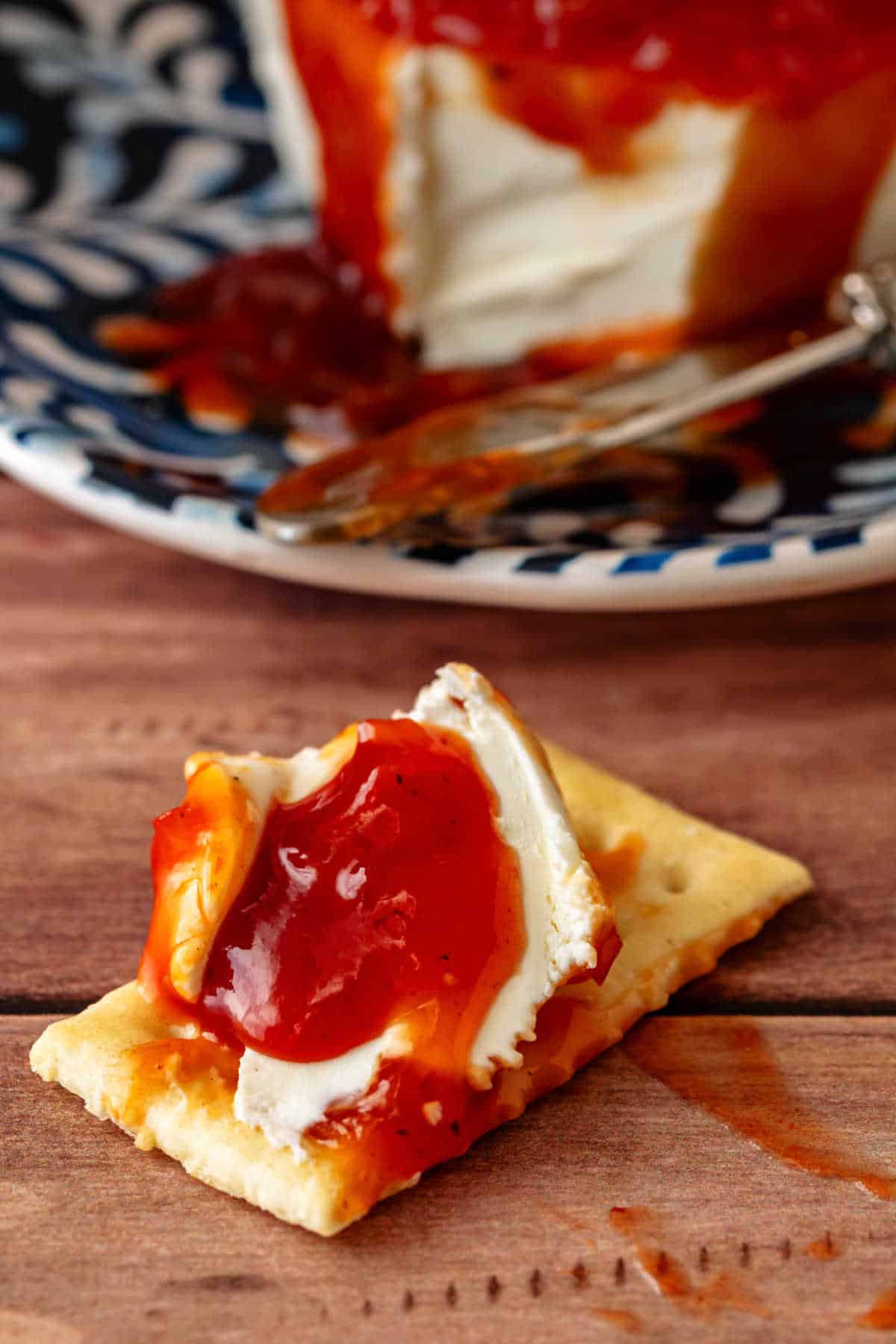 A closeup of a rectangular cracker topped with cream cheese and red sauce.