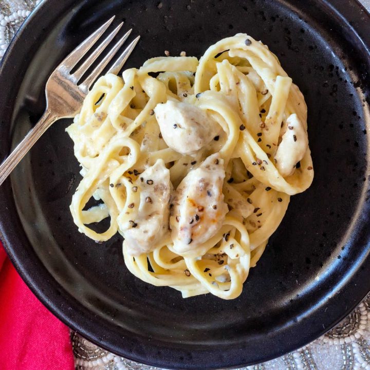 overhead shot of creamy pasta and chicken on a black plate
