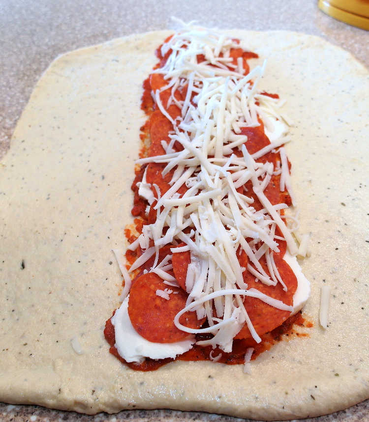 The cheese, pepperoni and sauce layered on dough for pepperoni bread.
