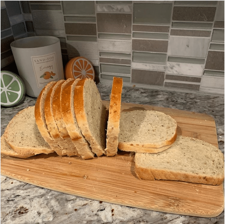 A wooden cutting board with a sliced loaf of bread on it. Some of the slices are lying down and others are still upright on the board.