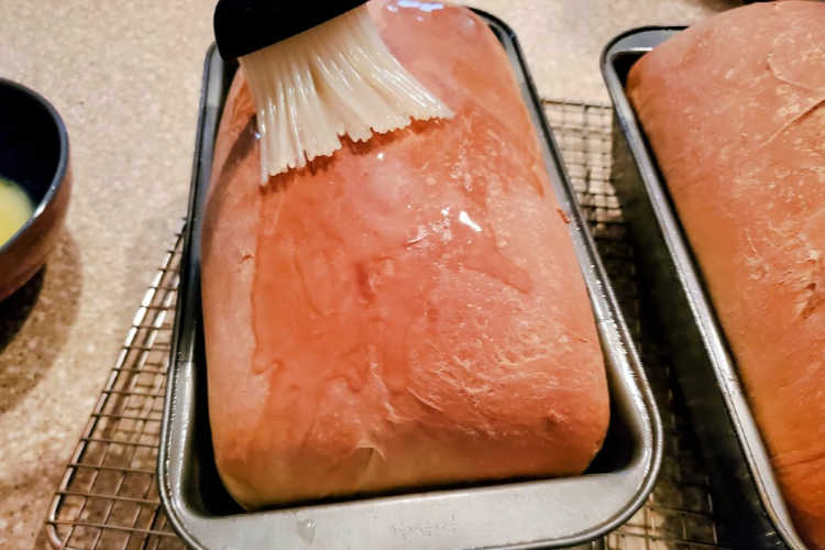 2 Loaves  of baked potato bread.  Melted butter being brushed on the brown crust.