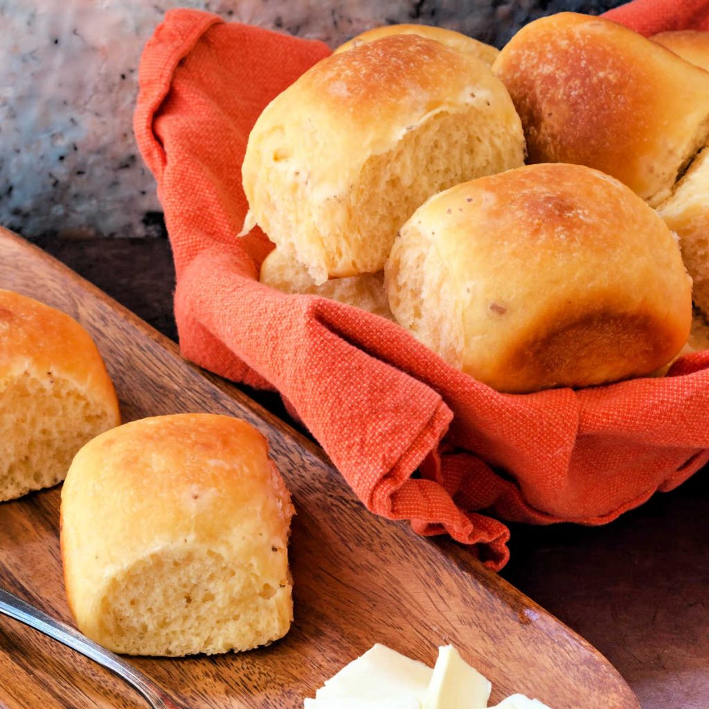 Bowl of rolls with 2 rolls on a wooden plate.