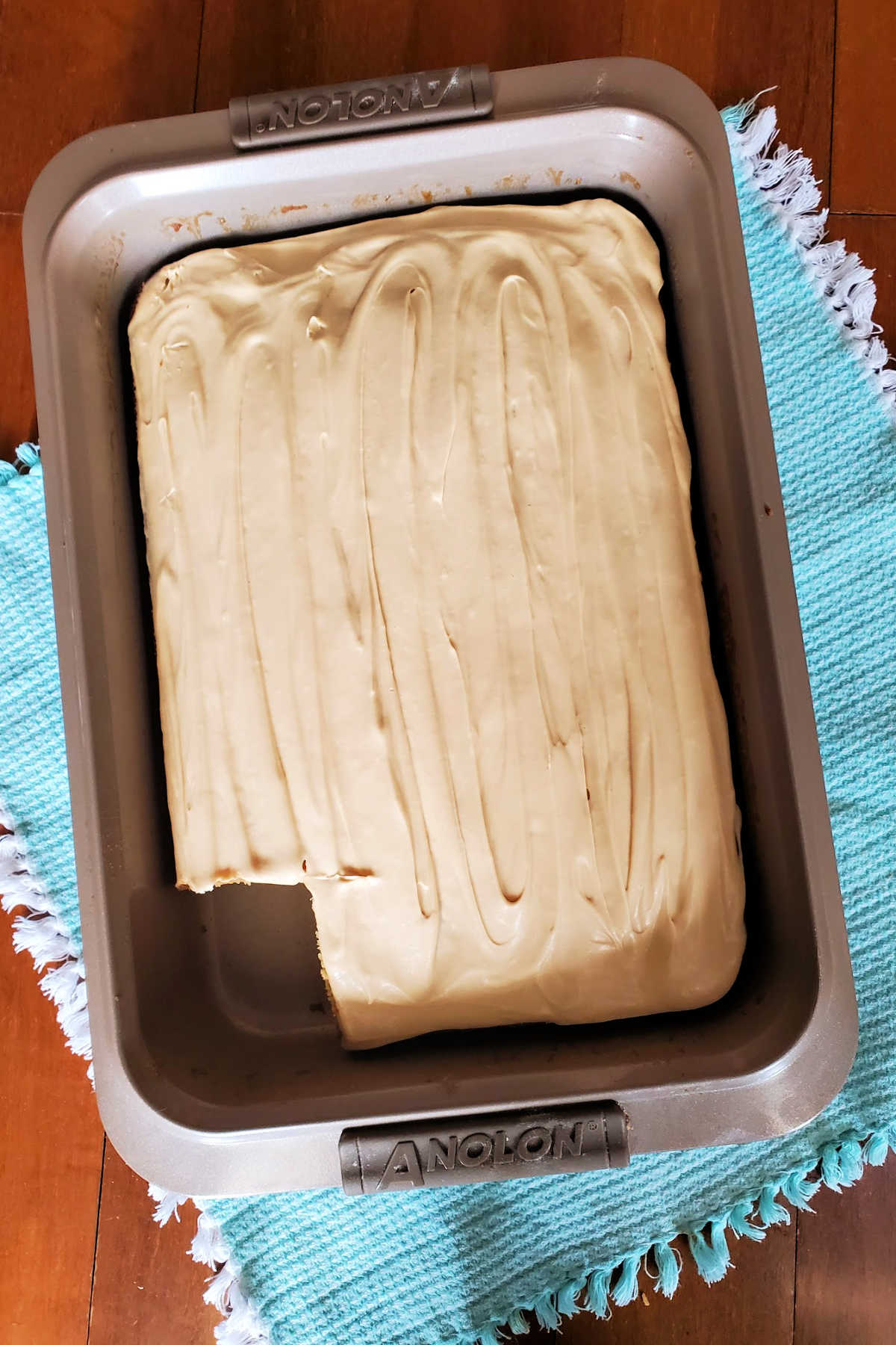 A whole butterscotch sheet cake with 1 slice cut out of it in a metal pan.