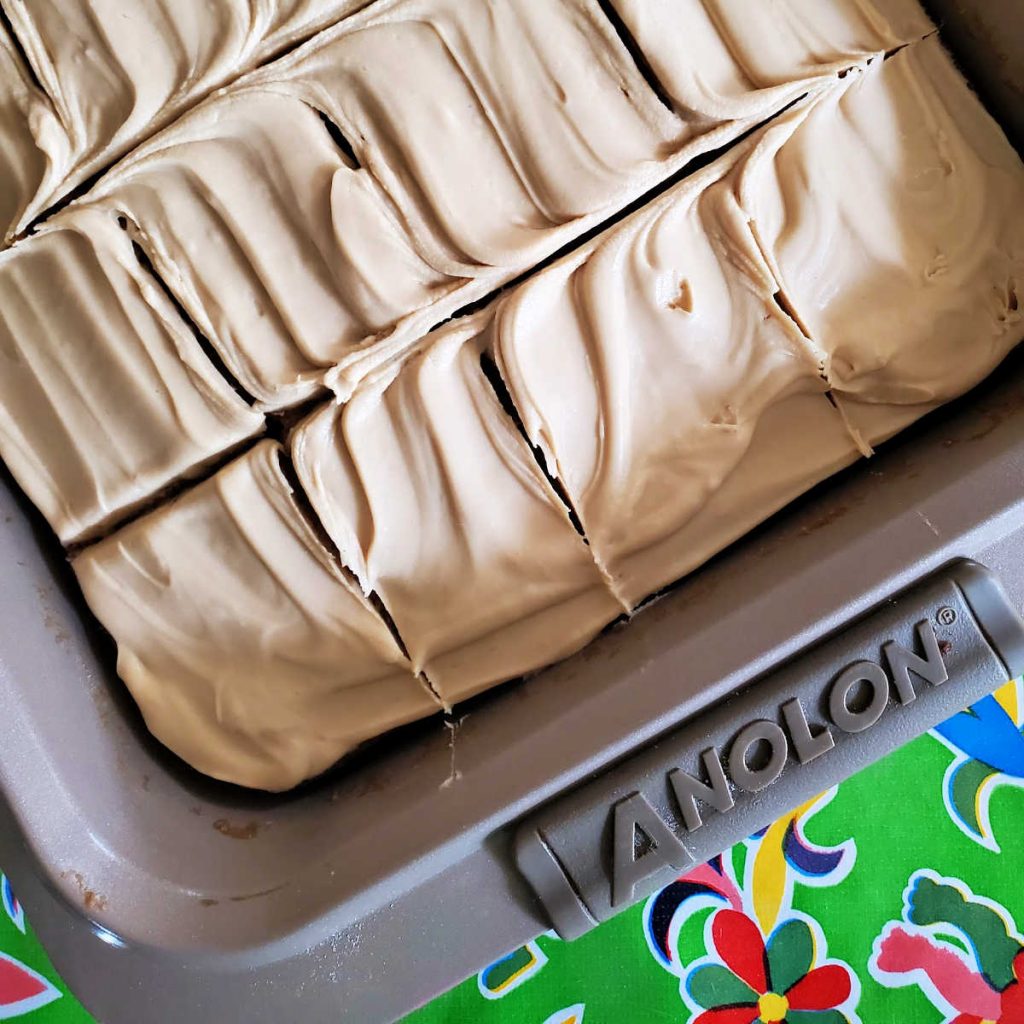 A frosted butterscotch sheet cake in a pan, showing cuts, ready for serving.