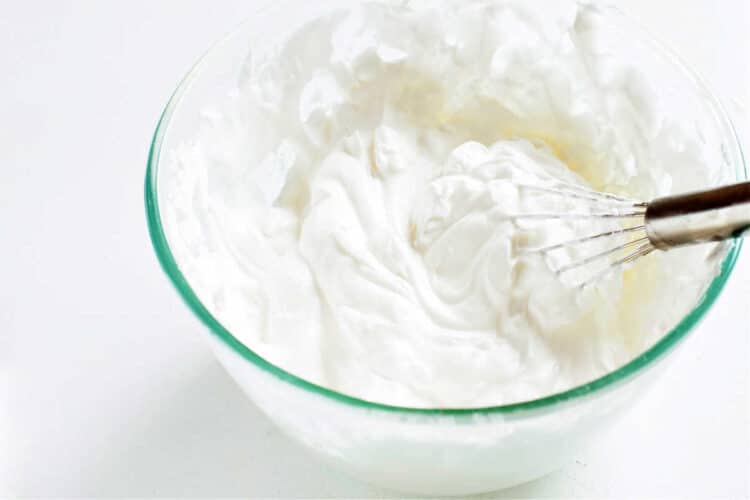 A glass bowl of whipped cream with a whisk in it.