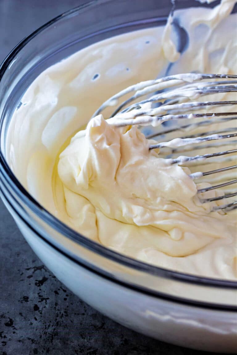 A high-angle shot of whipped cream in a glass bowl with a whisk.