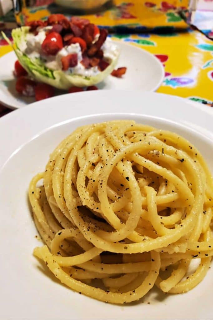 White plate with pasta and Parmesan cheese with wedge salad in the background.