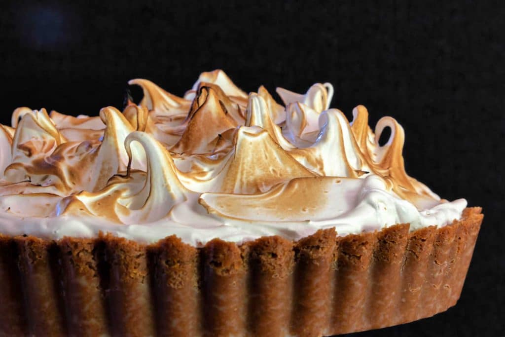 A close up of toasted meringue swirls and Graham cracker crust in a deep dish lemon meringue tart.