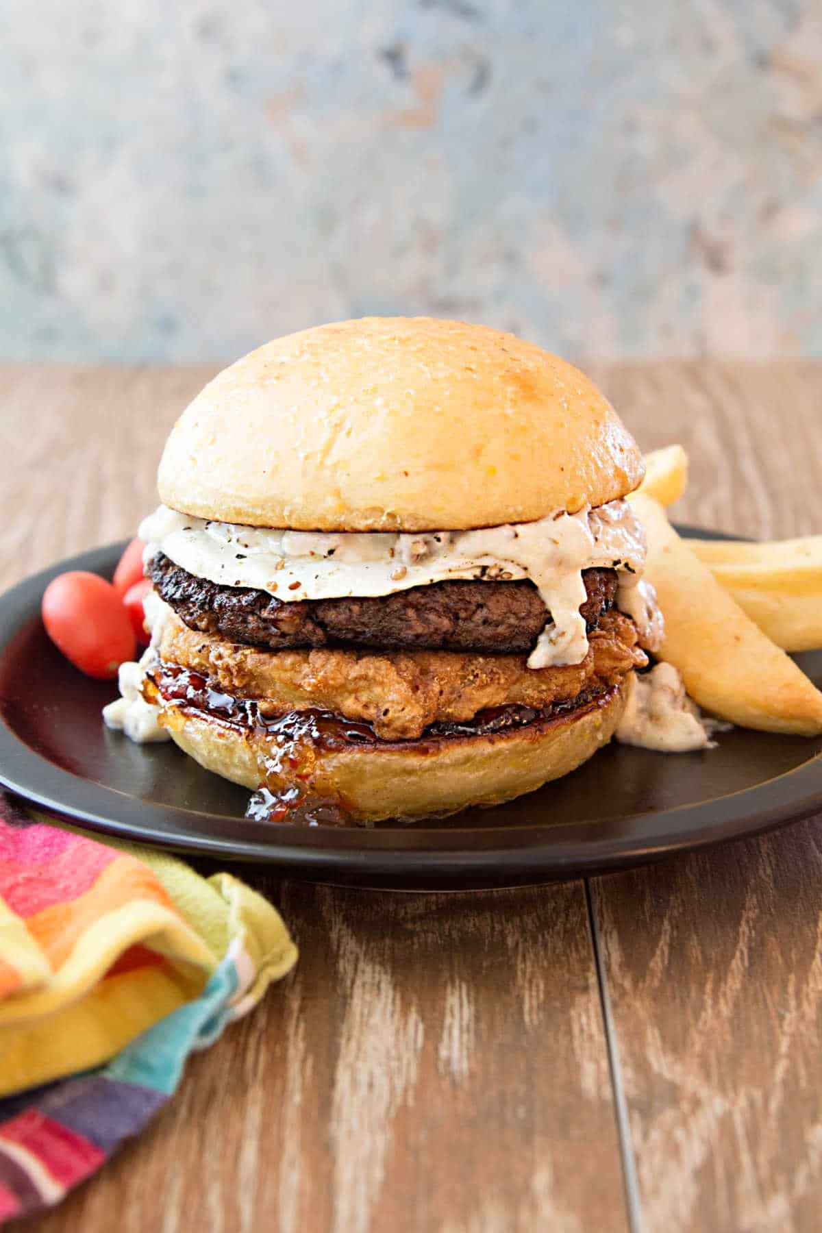 a breakfast burger on a plate with fries and grape tomatoes